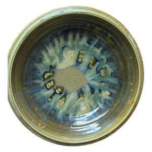 May include: A handmade ceramic bowl with a unique glaze. The bowl's exterior is a muted olive green, while the interior features a blend of blues, greens, and gold, creating a striking, organic pattern. The bowl is round and has a slightly textured rim.