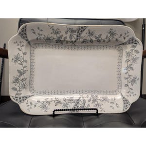 May include: A rectangular ceramic serving platter with rounded corners, featuring a white base and a dark gray floral pattern along the border. The design includes intricate botanical illustrations of flowers and leaves, complemented by a geometric lattice trim.