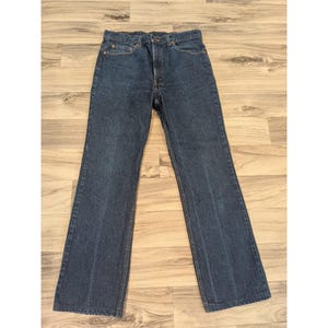 May include: A pair of dark blue denim jeans featuring a classic five-pocket design, a button fly closure, and a straight-leg cut. The fabric displays a uniform deep indigo wash with subtle fading along the seams and a standard waistband with belt loops.