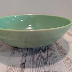 May include: A large, round, smooth-surfaced bowl in a solid light mint green color. The bowl features a wide, open top with a slightly tapered base and a glossy finish that reflects light across its interior and exterior curved walls.