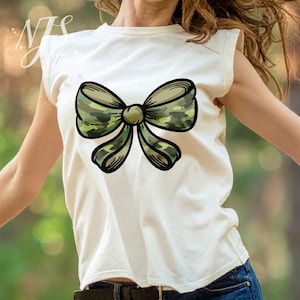 Könnte beinhalten: Ein cremefarbenes ärmelloses T-Shirt mit einem großen Schleifendesign. Die Schleife hat ein Camouflage-Muster in Grün-, Braun- und Beigetönen, umrandet in Schwarz. Das T-Shirt wird von einer Person getragen.