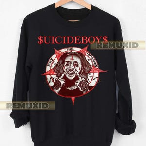 May include: Black sweatshirt with the red text "$UICIDEBOYS" above a graphic of a person with a cross on their forehead and a red star. The graphic also includes the words "THE POPULATION" and "FUCK".
