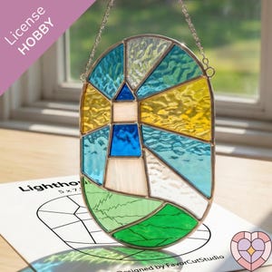 May include: Stained glass lighthouse window hanging with blue, yellow, and green panels. The lighthouse design is set in a silver-toned metal frame and suspended by a chain. The image includes the text "License HOBBY" and "Lighthouse 5x7".