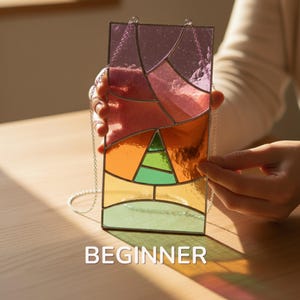 May include: A rectangular stained glass panel with a colorful geometric design. The panel features shades of pink, orange, green, and yellow, with a silver chain for hanging. The word "BEGINNER" is displayed at the bottom of the image.