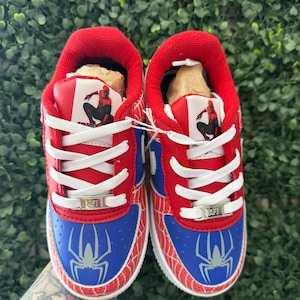 Puede incluir: Par de zapatillas rojas, azules y blancas con tem&aacute;tica de Spider-Man. Las zapatillas presentan un gr&aacute;fico de Spider-Man en el lateral y la leng&uuml;eta, con cordones blancos y suela blanca. Zapatos para ni&ntilde;os.