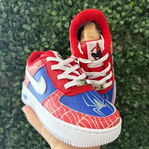 Puede incluir: Zapatillas rojas, azules y blancas con tem&aacute;tica de Spider-Man. Los zapatos presentan una puntera y un tal&oacute;n rojos, paneles laterales azules y un logotipo de Nike blanco. El dise&ntilde;o incluye un patr&oacute;n de telara&ntilde;a y un gr&aacute;fico de Spider-Man en la leng&uuml;eta.