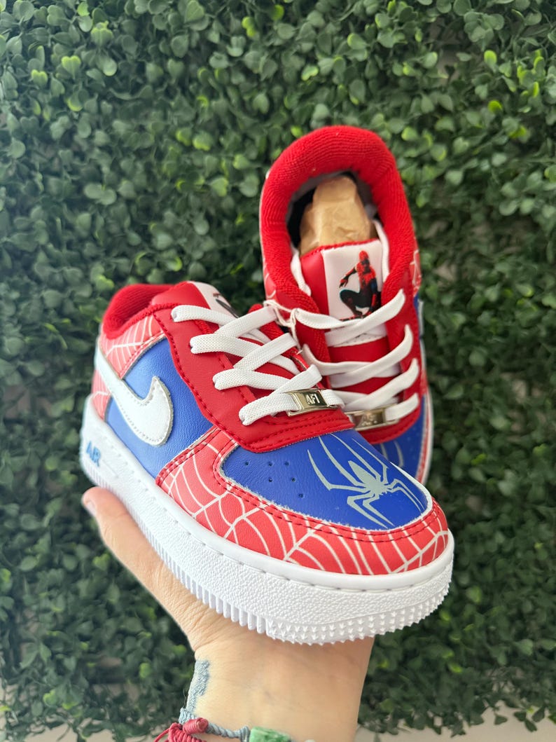Puede incluir: Zapatillas rojas, azules y blancas con tem&aacute;tica de Spider-Man. Los zapatos presentan una puntera y un tal&oacute;n rojos, paneles laterales azules y un logotipo de Nike blanco. El dise&ntilde;o incluye un patr&oacute;n de telara&ntilde;a y un gr&aacute;fico de Spider-Man en la leng&uuml;eta.