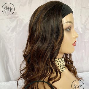 May include: A mannequin head showcasing a brown wig with highlights and a wavy texture. The wig is styled with a black headband. The mannequin is wearing a leopard print scarf.