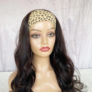 May include: A mannequin head showcasing a dark brown wig with long, wavy hair. The wig includes a headband with a tan leopard print design. The mannequin has a neutral expression, set against a white backdrop.