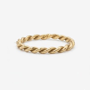 Könnte beinhalten: Ein goldener Ring mit einem durchgehenden gedrehten Seildesign. Das Band hat eine polierte metallische Oberfläche mit einem sich wiederholenden Spiralmuster, das ein strukturiertes Aussehen um den gesamten Umfang des Schmuckstücks erzeugt.