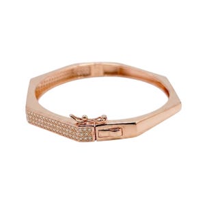 Pode incluir: Pulseira em tom de ouro rosa com um design geom&eacute;trico. A pulseira apresenta um fecho retangular e uma se&ccedil;&atilde;o incrustada com pequenas pedras preciosas transparentes. A pulseira foi projetada para ser usada ao redor do pulso.