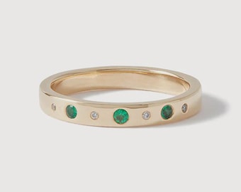 Puede incluir: Un anillo de banda de oro con una serie de esmeraldas verdes redondas y diamantes blancos transparentes más pequeños engastados a ras, alternándose en la superficie exterior. El metal tiene un acabado pulido y las piedras están incrustadas.