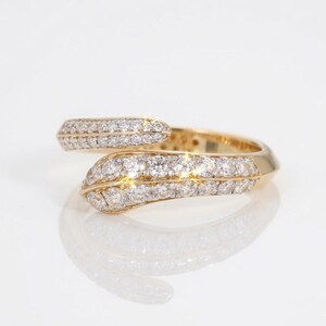 Puede incluir: Un anillo de estilo bypass elaborado en oro amarillo pulido, con dos extremos superpuestos incrustados con numerosos diamantes pequeños, redondos y transparentes en pavé que se extienden a lo largo de la banda, creando un efecto brillante.