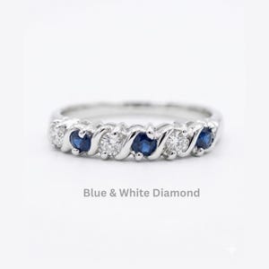 Puede incluir: Un anillo de tono plateado con un patrón alterno de piedras redondas azules y piedras blancas transparentes engastadas en una banda continua. La banda de metal tiene un diseño trenzado en forma de onda entre cada piedra. El texto Blue & White Diamond es visible.
