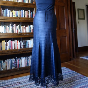 May include: A long, dark blue skirt with a mermaid-style hemline. The skirt is made of a textured fabric and has a lace trim at the bottom.