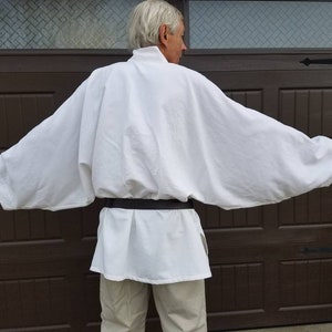 May include: A white tunic with long sleeves and a black belt. The tunic is made of a soft, flowing fabric and has a simple, elegant design.