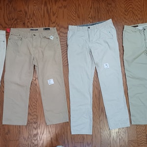 May include: Five pairs of beige and white pants laid out on a wooden floor. The pants are numbered 1 through 5.