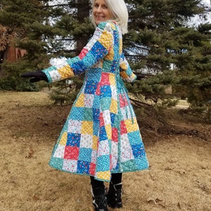 May include: A colorful patchwork coat with a quilted design. The coat features a variety of squares in blue, yellow, red, and green floral patterns. The coat has long sleeves and a flared skirt, perfect for a unique style.