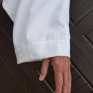 May include: A white long-sleeved shirt with a folded cuff. The shirt is made of a smooth, wrinkle-resistant fabric.