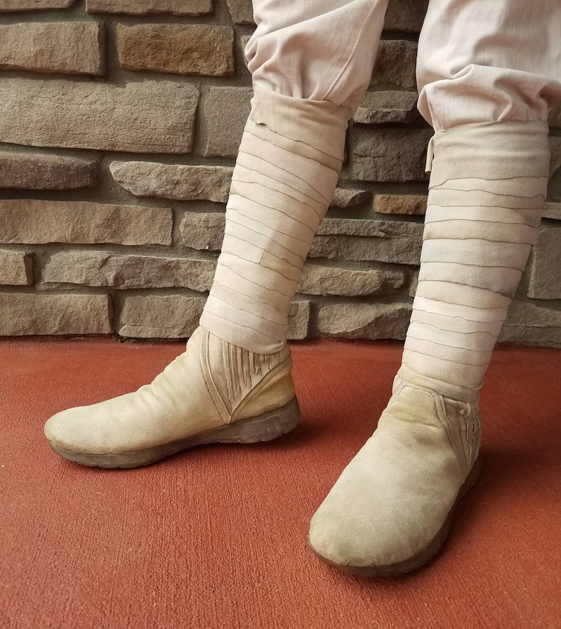 May include: A pair of white suede boots with a unique design featuring multiple straps. The boots are worn and have a distressed look.