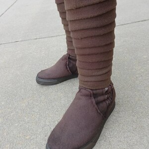 May include: Brown fabric boots with a unique layered design. The boots have a black rubber sole and a rounded toe.
