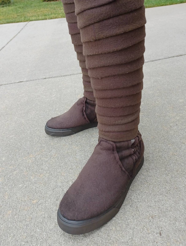 May include: Brown fabric boots with a unique layered design. The boots have a black rubber sole and a rounded toe.