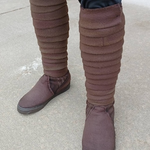 May include: A pair of brown suede boots with a layered design. The boots are worn and have a distressed look.