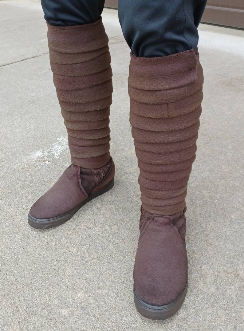May include: A pair of brown suede boots with a layered design. The boots are worn and have a distressed look.