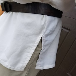 May include: A white long-sleeved shirt with a brown leather belt. The shirt has a side slit on the right side.