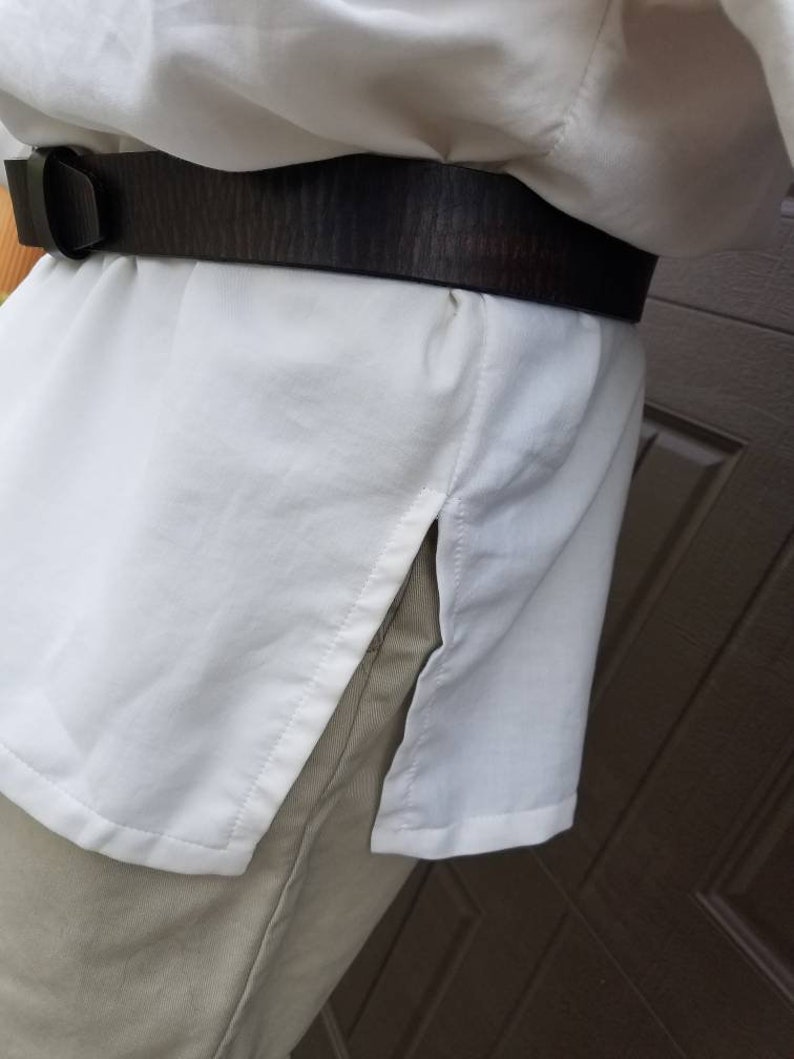 May include: A white long-sleeved shirt with a brown leather belt. The shirt has a side slit on the right side.