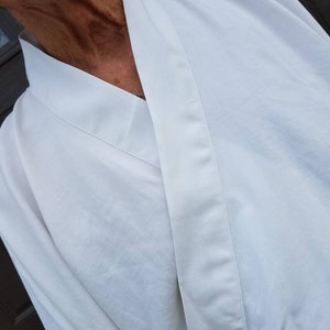 May include: A white robe with a long, pointed collar and a single button closure. The robe is made of a soft, lightweight fabric.