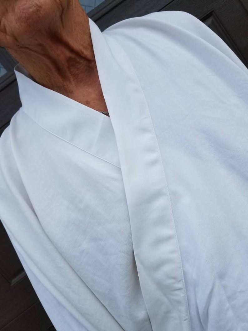 May include: A white robe with a long, pointed collar and a single button closure. The robe is made of a soft, lightweight fabric.