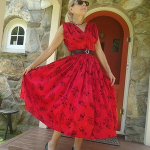 May include: A red sleeveless dress with a black floral print and a brown belt. The dress has a full skirt and a V-neckline.