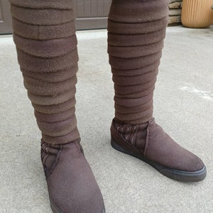 May include: A pair of brown felt boots with a layered design on the shaft. The boots have black soles and are worn on a person's feet.