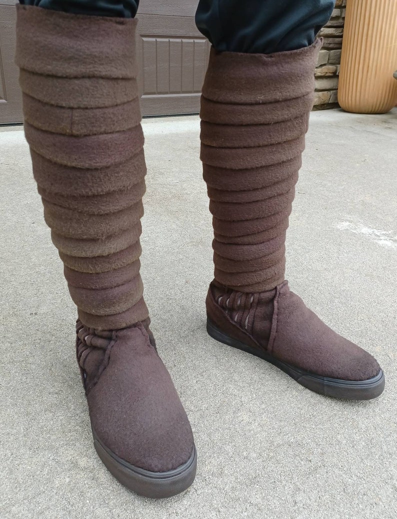 May include: A pair of brown felt boots with a layered design on the shaft. The boots have black soles and are worn on a person's feet.