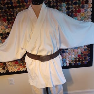 May include: A white robe with a brown belt. The robe has a wide, open collar and long sleeves. The belt is made of leather and has a buckle.