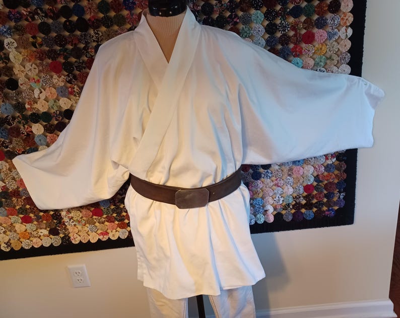 May include: A white robe with a brown belt. The robe has a wide, open collar and long sleeves. The belt is made of leather and has a buckle.