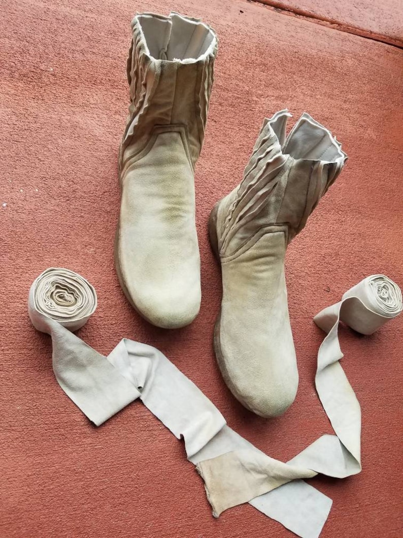 May include: Two pairs of beige suede boots with a zipper on the side. The boots are on a red surface with two beige suede straps.