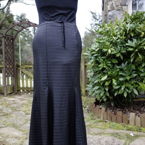 May include: A black maxi skirt with a ribbed texture and a lace trim. The skirt is fitted at the waist and flares out at the hem.