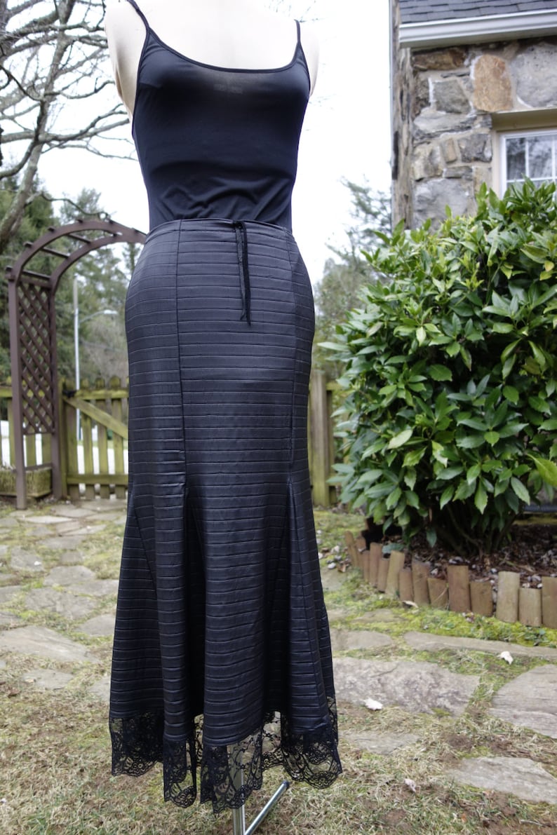 May include: A black maxi skirt with a ribbed texture and a lace trim. The skirt is fitted at the waist and flares out at the hem.
