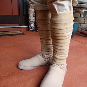 May include: Beige boots with a layered, folded design on the shaft. The boots are made of a soft, fuzzy material and have a white sole.