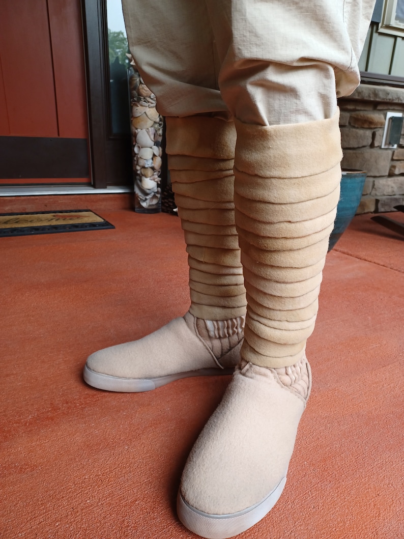 May include: Beige boots with a layered, folded design on the shaft. The boots are made of a soft, fuzzy material and have a white sole.