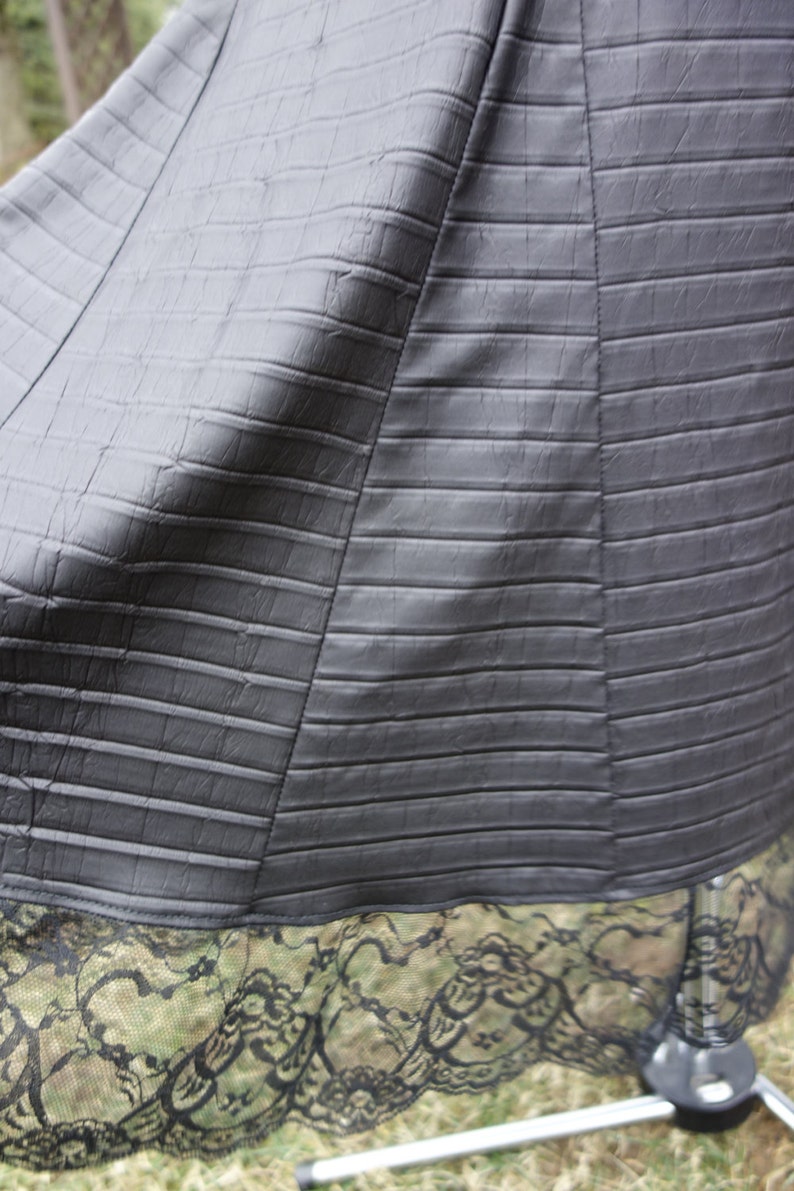 May include: A black skirt with a textured, alligator-like pattern. The skirt has a black lace trim.