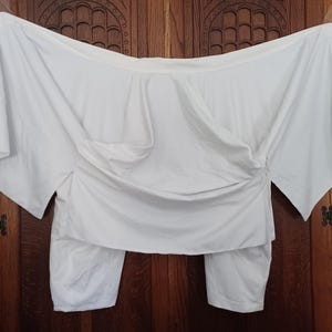 May include: A white, off-the-shoulder top with long sleeves and a gathered, draped design. The top is made of a lightweight fabric and has a relaxed fit.