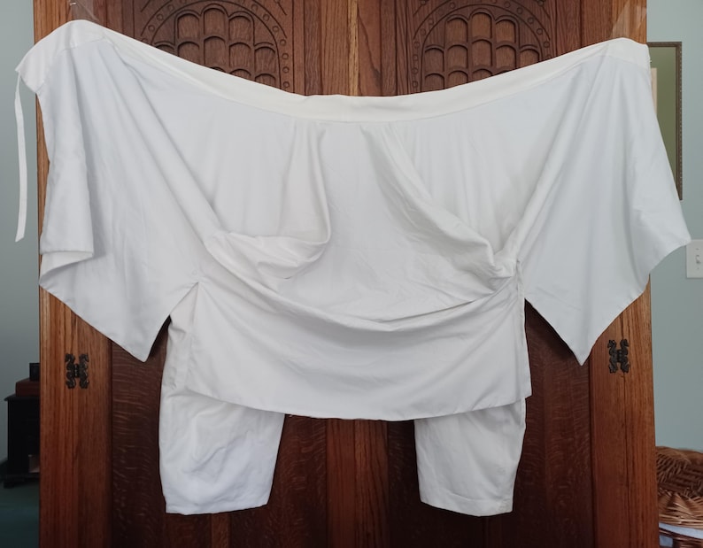 May include: A white, off-the-shoulder top with long sleeves and a gathered, draped design. The top is made of a lightweight fabric and has a relaxed fit.
