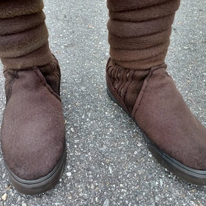 May include: A pair of brown suede boots with a fold-over cuff. The boots have a black rubber sole.