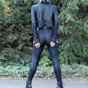 May include: A black leather cropped jacket with a ruffled hem and a black belt. The jacket is worn over black leggings.