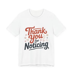 Puede incluir: Camiseta blanca con la frase "Thank You for Noticing" en letras rojas y azul marino. El diseño incluye estrellas, corazones y adornos. Una camiseta informal para el día a día.