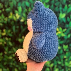 May include: A handmade blue and white plush toy, resembling a cartoon character. The plush has a rounded body, small arms, and a distinctive head shape. The toy is made of a soft, textured material.