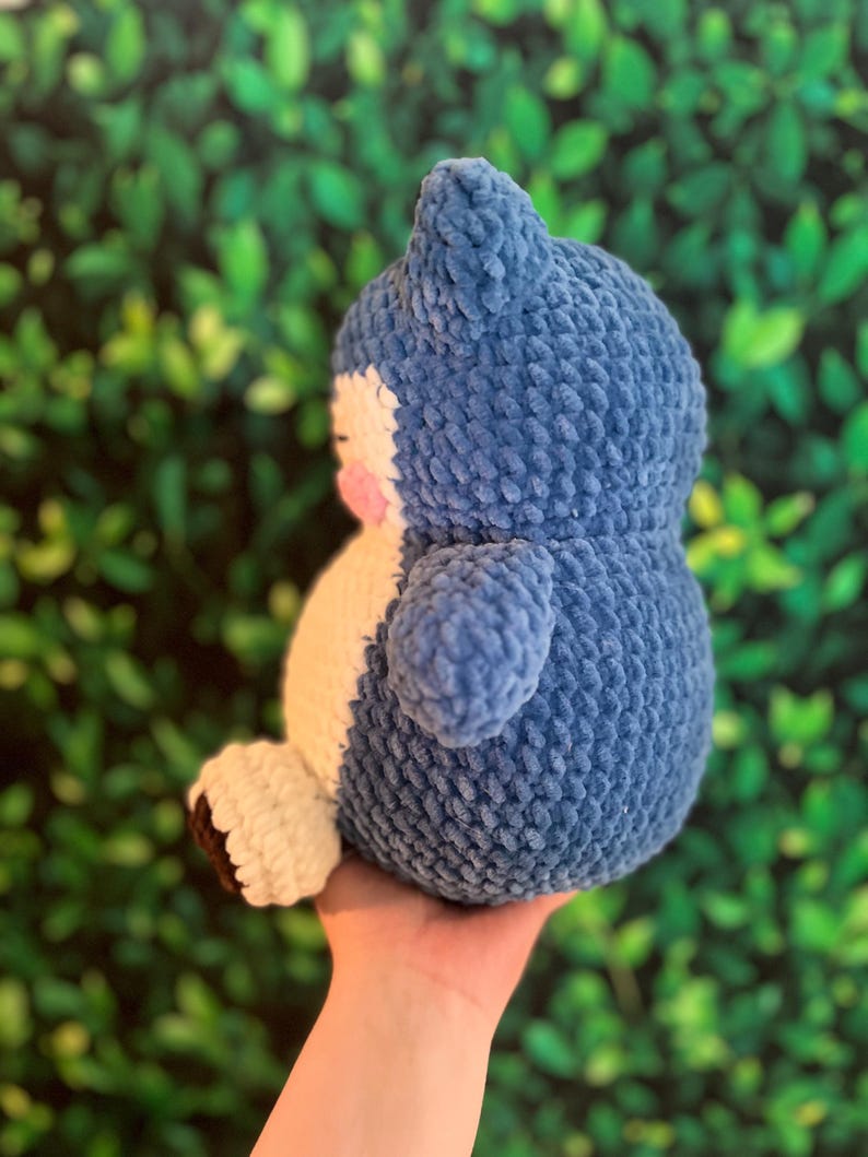 May include: A handmade blue and white plush toy, resembling a cartoon character. The plush has a rounded body, small arms, and a distinctive head shape. The toy is made of a soft, textured material.